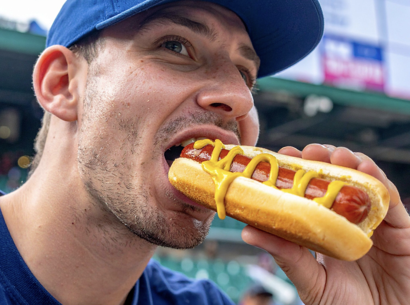 man biting into a hot dog on a bun with mustard